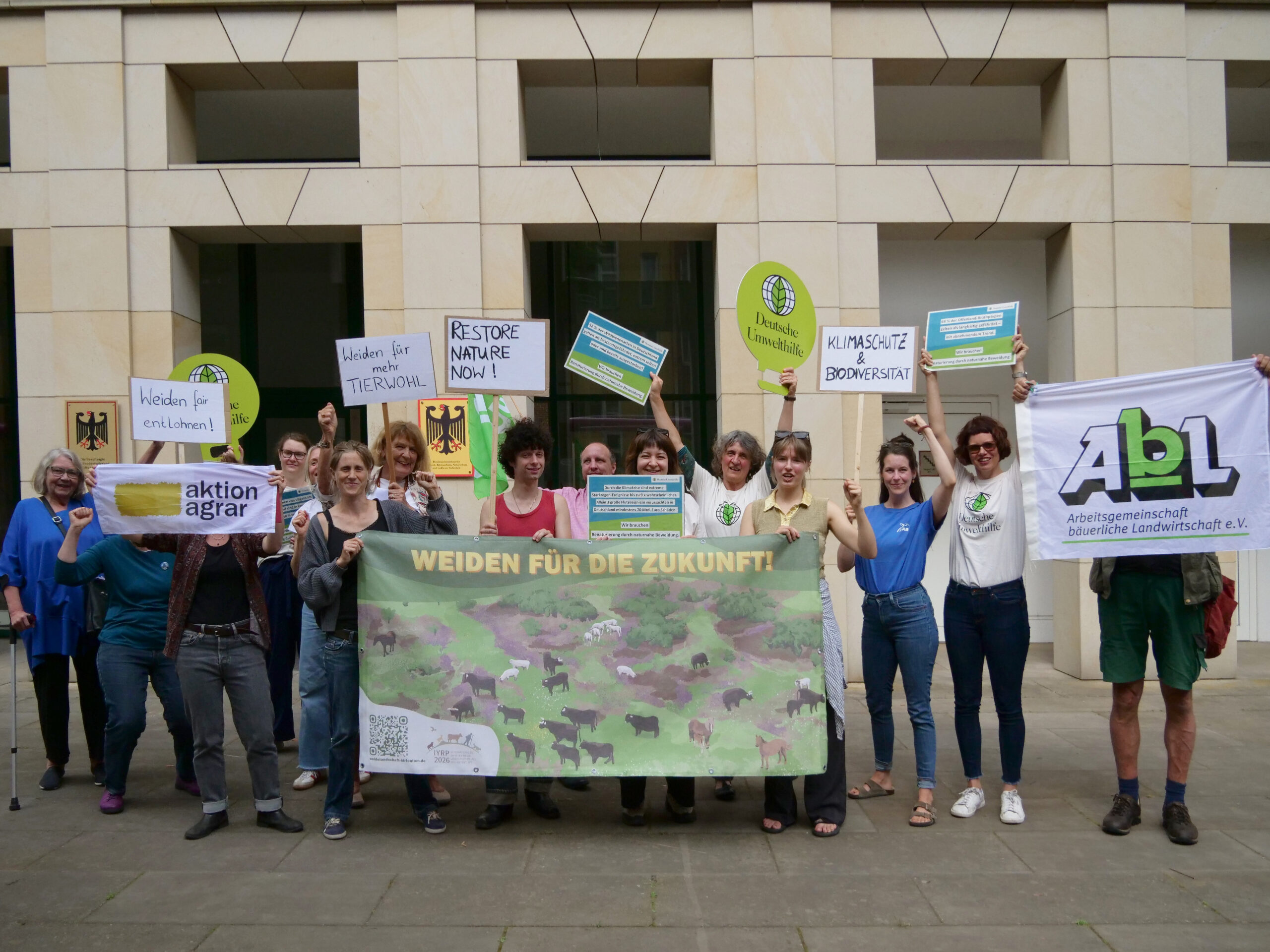 Menschen stehen mit einem großen Banner und vielen schildern protestierend.